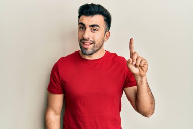 Bir fikir veya soruyla gülümseyen gündelik kıyafetler giyen genç İspanyol adam, bir numara, mutlu bir yüzle işaret ediyor. 