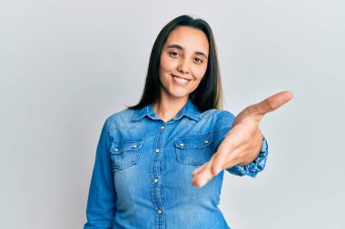 Sıradan bir kot ceket giyen genç İspanyol kadın dostça bir selamlama ve hoş geldin hediyesi olarak el sıkışırken gülümsüyor. başarılı iş. 