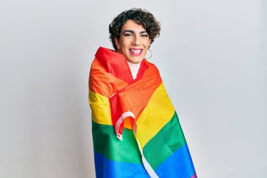 Gökkuşağı lgbtq bayrağına sarılmış, mutlu ve havalı bir gülümsemeyle gülümseyen kadın makyajı yapan genç bir adam. diş gösterme. 