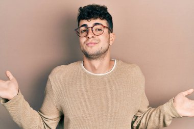 Sıradan kıyafetler giyen, gözlüklü, kafası karışık, elleri ve kolları havada bir İspanyol. şüphe kavramı. 