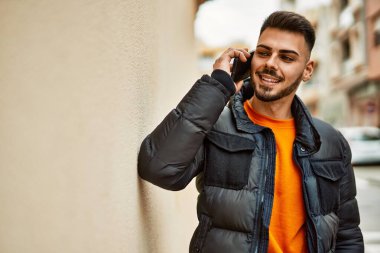 Yakışıklı, sakallı, mutlu, kendine güvenen, kışlık palto giymiş telefonda konuşan bir İspanyol.