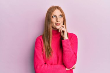 Genç İrlandalı kadın gündelik giysiler giyer şüphe üzerine yoğunlaşır çene üstüne parmak ve merak içinde yukarı bakar. 