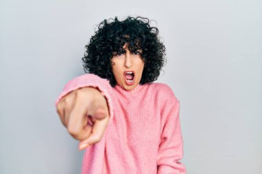 Orta Doğulu genç bir kadın, sıradan kıyafetler giyip kameraya kızgın ve sinirli bir şekilde seni işaret ediyor. 