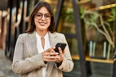 Genç İspanyol iş kadını şehirde akıllı telefon kullanarak mutlu gülümsüyor..
