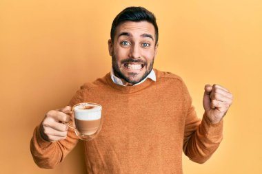 Genç İspanyol adam elinde kahveyle gururla bağırıyor zaferi kutluyor ve başarıyı kollarını kaldırarak kutluyor. 