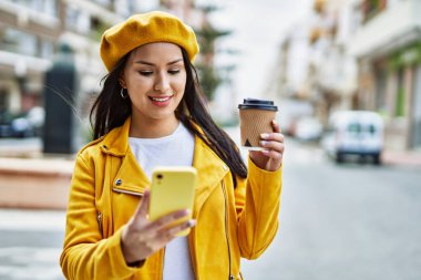 Genç Latin kız şehirde kahve içerek akıllı telefon kullanıyor..