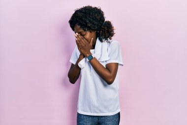 Genç Afro-Amerikalı kadın spor giyer ve ağlarken yüzünü ellerle kapatan üzgün bir yüz ifadesiyle havlu giyer. depresyon kavramı. 