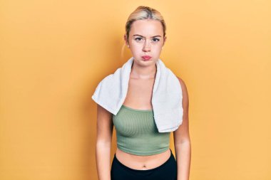 Spor kıyafetleri giyen ve havluyla yanak şişiren komik yüzlü genç sarışın kız. Havayla şişmiş ağız, çılgın bir ifade.. 
