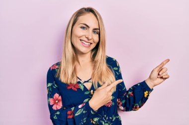 Gündelik kıyafetler giyen, gülümseyen ve kameraya bakan genç beyaz bir kadın iki elini ve parmağını yana doğru uzattı.. 