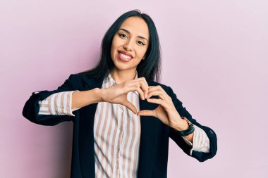 İş elbiseleri giyen, aşık gülümseyen, elleriyle kalp sembolü yapan genç İspanyol kız. romantik kavram. 