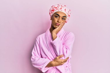 Duş havlusu şapkası ve bornoz giyen İspanyol adam kollarını kavuşturup depresyondan sıkılmış ve yorgun göründüğünü düşünüyor.. 