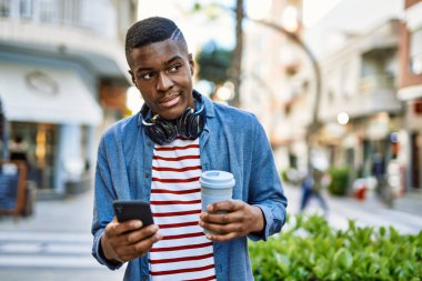 Genç Afrikalı Amerikalı adam akıllı telefon kullanıyor. Şehirde kahve içiyor..