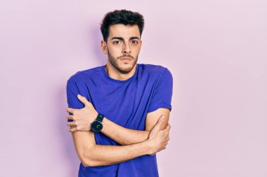 Latin asıllı genç bir adam günlük tişört giyiyor. Kış soğuğu için titriyor ve donuyor. Yüzünde üzgün ve şok ifadesi var. 