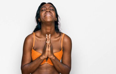 Genç Afro-Amerikalı kadın iç çamaşırı giyip elleri bağlı yalvarıyor ve dua ediyor. Yüzünde umut ifadesi var. Çok duygusal ve endişeli. Yalvarıyor. 