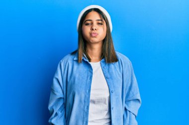 Şirin yün şapkalı, komik yüzlü, yanak şişiren genç Latin kadın. Havayla şişmiş ağız, çılgın bir ifade.. 