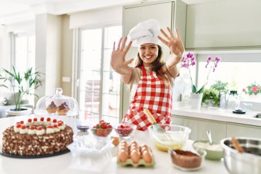 Güzel, genç, esmer pasta şefi kadın mutfakta hamur işleri pişirirken dokuz numaralı parmaklarıyla işaret ederken kendinden emin ve mutlu gülümsüyor.. 