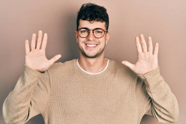 Gündelik kıyafetler giyen ve gözlük takan İspanyol genç adam on numarayı gösterip işaret ederken kendinden emin ve mutlu gülümsüyor.. 