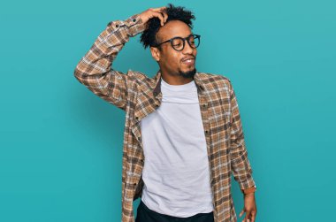 Sakallı, günlük kıyafetler ve gözlüklü, kendine güvenen, el hareketleriyle saçlarına dokunan çekici ve modaya uygun poz veren Afro-Amerikan genç adam. 