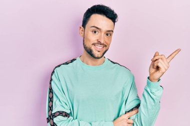 Gündelik kıyafetler giyen genç İspanyol adam gülümsüyor mutlu bir şekilde elini ve parmağını yana uzatıyordu. 