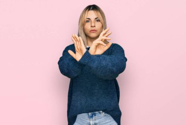 Gündelik kıyafetler giyen beyaz bir kadın. Reddedilmiş yüz ifadesi. Kollarını kavuşturup, avuçlarını çaprazlayarak negatif işaret veriyor. 