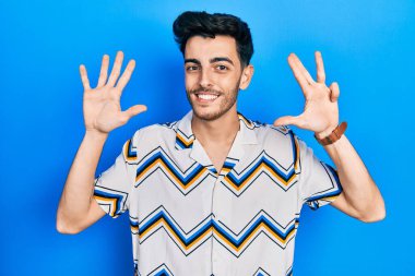 Gündelik kıyafetler giyen genç İspanyol adam dokuz numarayı gösterip işaret ederken kendinden emin ve mutlu bir şekilde gülümsüyor.. 