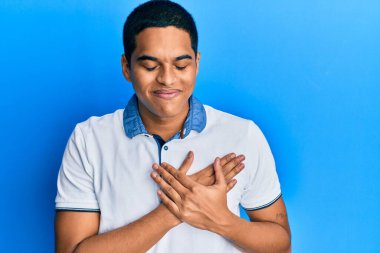 Gündelik kıyafetler giyen, göğsünde elleri, yüzünde minnet dolu bir jestle gülümseyen genç, yakışıklı İspanyol bir adam. sağlık kavramı. 