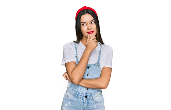 若いヒスパニック系の女の子の質問については 集中的な表現を考えて顎に手でカジュアルな服を着て 思慮深い顔で笑顔 疑わしい概念 — ストック写真