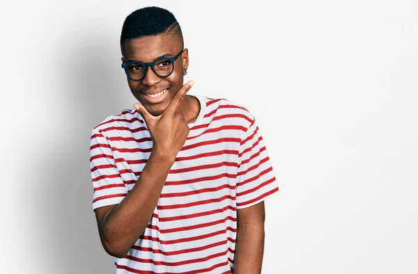 カジュアルなTシャツを着た若いアフリカ系アメリカ人の男性と カメラを見て自信を持っている眼鏡が交差した腕と手であごを上げて笑っている ポジティブな — ストック写真