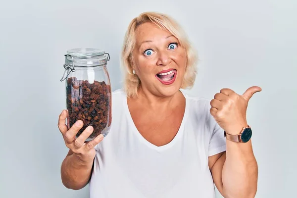 Middle Age Blonde Woman Holding Raisins Bowl Pointing Thumb Side — Stock Photo, Image