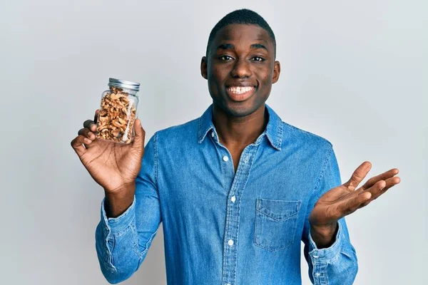 Joven Afroamericano Sosteniendo Tarro Con Nueces Celebrando Logro Con Sonrisa — Foto de Stock