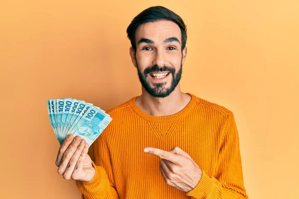 Νεαρός Ισπανός Κρατώντας 100 Βραζιλιάνικα Αληθινά Χαρτονομίσματα Χαμογελώντας Χαρούμενος Δείχνοντας — Φωτογραφία Αρχείου