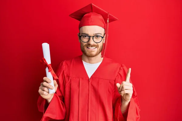 Νεαρός Κοκκινομάλλης Που Φοράει Καπέλο Αποφοίτησης Και Ρόμπα Τελετής Κρατώντας — Φωτογραφία Αρχείου