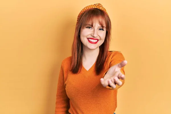 红头发的年轻女人穿着休闲的橙色毛衣 友善地微笑 握手致意和欢迎 成功的商业 — 图库照片