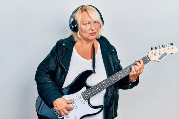 Medelålders Blond Kvinna Spelar Elgitarr Med Hörlurar Skeptisk Och Nervös — Stockfoto