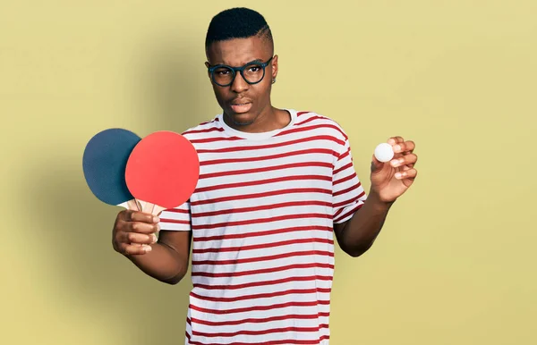 年轻的非洲裔美国人手里拿着红乒乓球球拍和毫无头绪的混乱表情 怀疑概念 — 图库照片