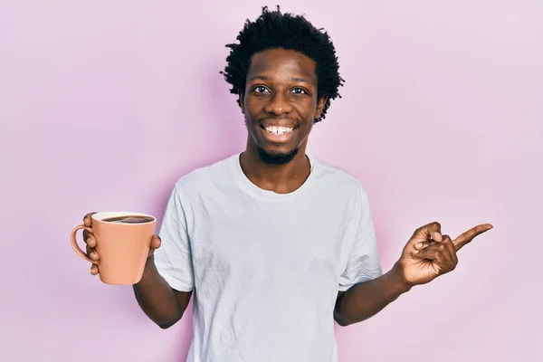 年轻的非洲裔美国人 拿着一杯咖啡 高兴地微笑着 手指手画脚地指向一边 — 图库照片