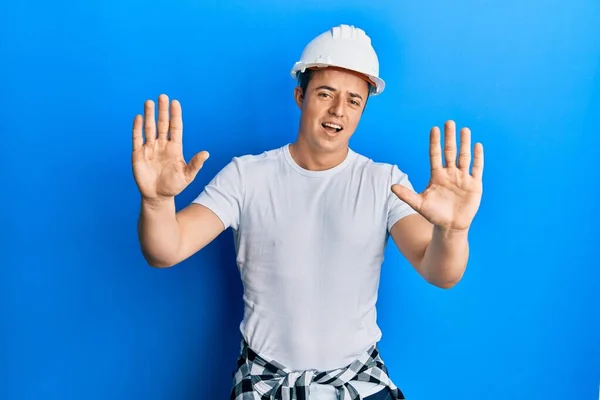 英俊的年轻人穿着建筑工人制服 头戴硬礼帽 手拿着恐惧的表情 害怕地停止手势 震惊地大叫 恐慌概念 — 图库照片