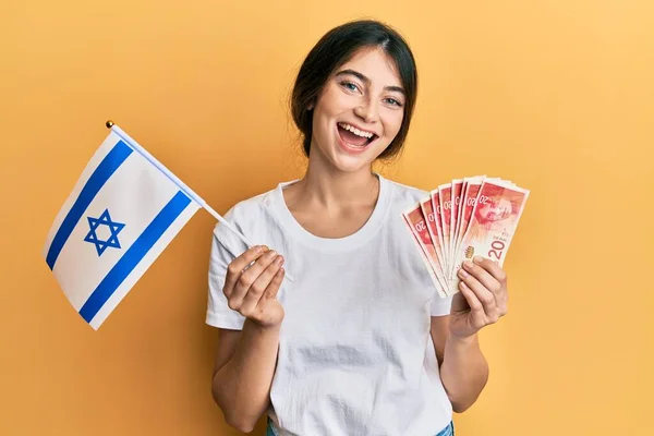 年轻的高加索女人拿着以色列国旗和先令钞票 笑得很开心 笑得很大声 因为有一个可笑的疯狂笑话 — 图库照片