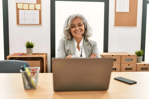 中年女商人坐在办公桌前工作 在办公室里用笔记本电脑开心地微笑着 双臂交叉地看着相机 积极的人 — 图库照片