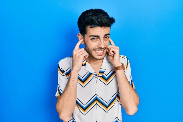 大音量の音楽のノイズのためにいらいらする表情で指で耳を覆うカジュアルな服を着た若いヒスパニック系の男 聴覚障害の概念 — ストック写真