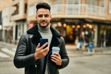 Genç Arap adam akıllı telefon kullanıyor ve şehirde kahve içiyor..