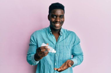 Yakışıklı siyah adam el dezenfektanı jeli kullanıyor kameraya seksi bir ifadeyle bakıyor, neşeli ve mutlu bir yüzle.. 