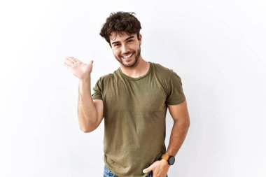 İzole edilmiş beyaz arka planda duran İspanyol adam mutlu bir şekilde sunum yapıyor ve avuç içiyle kameraya bakıyor.. 