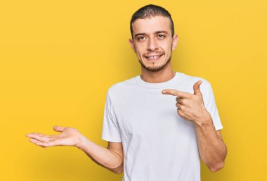 Latin asıllı beyaz tişört giyen genç adam kameraya hayret ediyor ve gülümsüyor.. 