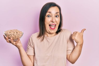 Orta yaşlı, İspanyol bir kadın elinde nohut kasesi, başparmağıyla yan tarafa bakıyor ve ağzı açık gülümsüyor. 