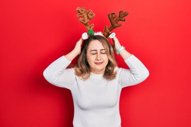 Orta yaşlı, beyaz, şirin Noel geyiği boynuzları takan, baş ağrısı çeken, çaresiz ve stresli bir kadın. Çünkü acı ve migren. Eller başının üstünde.. 