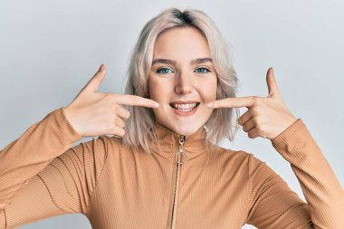 Sıradan kıyafetler giyen, neşeli gülümseyen, parmaklarıyla ve ağzıyla işaret eden genç sarışın kız. diş sağlığı kavramı. 