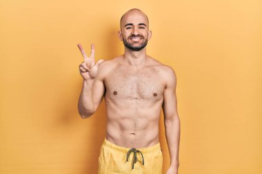 Mayo giyen genç kel adam üç numarayı gösterip işaret ederken kendinden emin ve mutlu gülümsüyor.. 