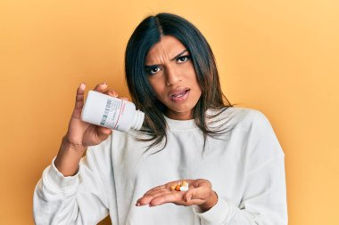 Genç Latin transseksüel kadın elinde şok edici bir yüz ifadesi olan haplar tutuyor. Şüpheci ve alaycı görünüyor, ağzı açık kalınca şaşırıyor. 