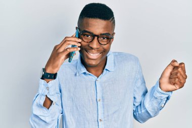 Genç Afrikalı Amerikalı adam akıllı telefonda konuşuyor gururla bağırıyor, zaferi kutluyor ve kollarını kaldırarak çok heyecanlı bir şekilde. 
